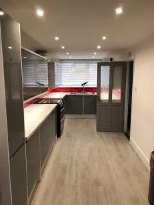 Complete kitchen renovation in Basildon featuring gloss grey and white units, a striking red tiled splashback, and an extended breakfast bar for added space.